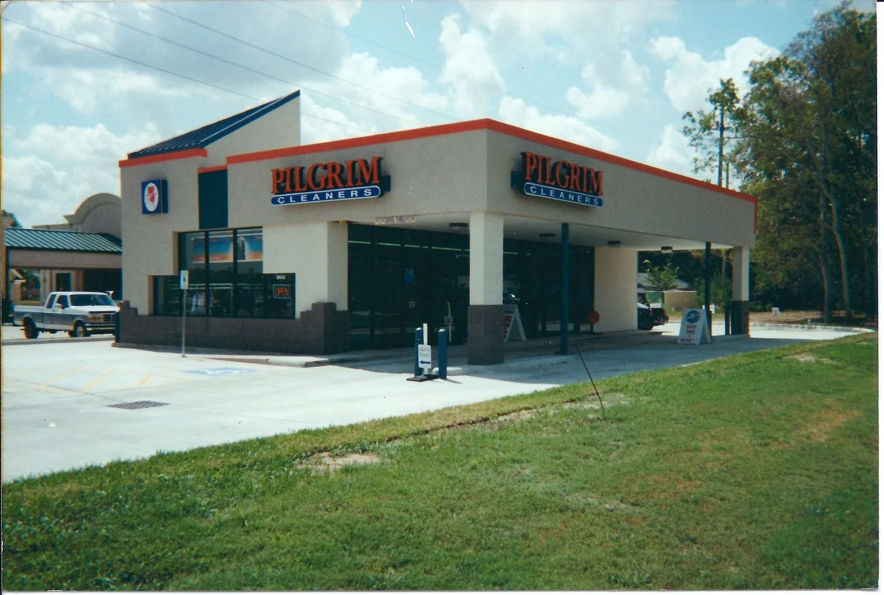 Pilgrim Cleaners storefront with red and blue signs and a covered drive-through